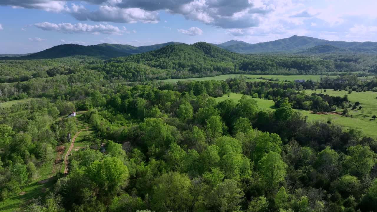 Aerial establishing shot of green lush forest landscape with mountains and small house in suburb. American suburb district with clouds at sky. Wide shot.