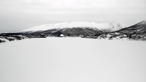 Drone-shot-of-a-frozen-lake-surrounded-by-mountains-in-Tromso,-Norway-during-winter