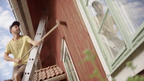 hombre en la escalera quita la pintura roja vieja de la pared de madera exterior