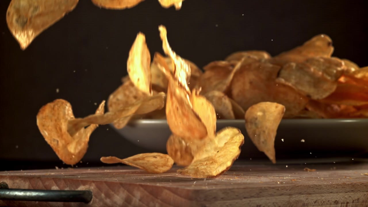 Crispy Potato Chips Falling in Slow Motion onto a Wooden Table
