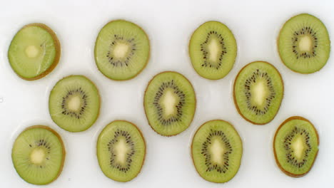 water splashes in slow motion. top view: several circles of kiwi is washed with water on a white background. chopped fruit.