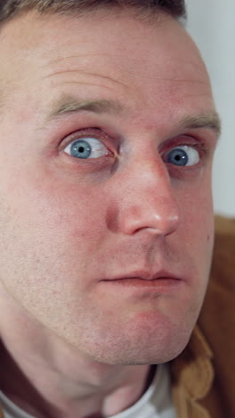 portrait of a funny freelancer. young man blinking eyes madly after sitting at home for a long period. amusing man with a laptop on table in the kitchen. lockdown concept. vertical video