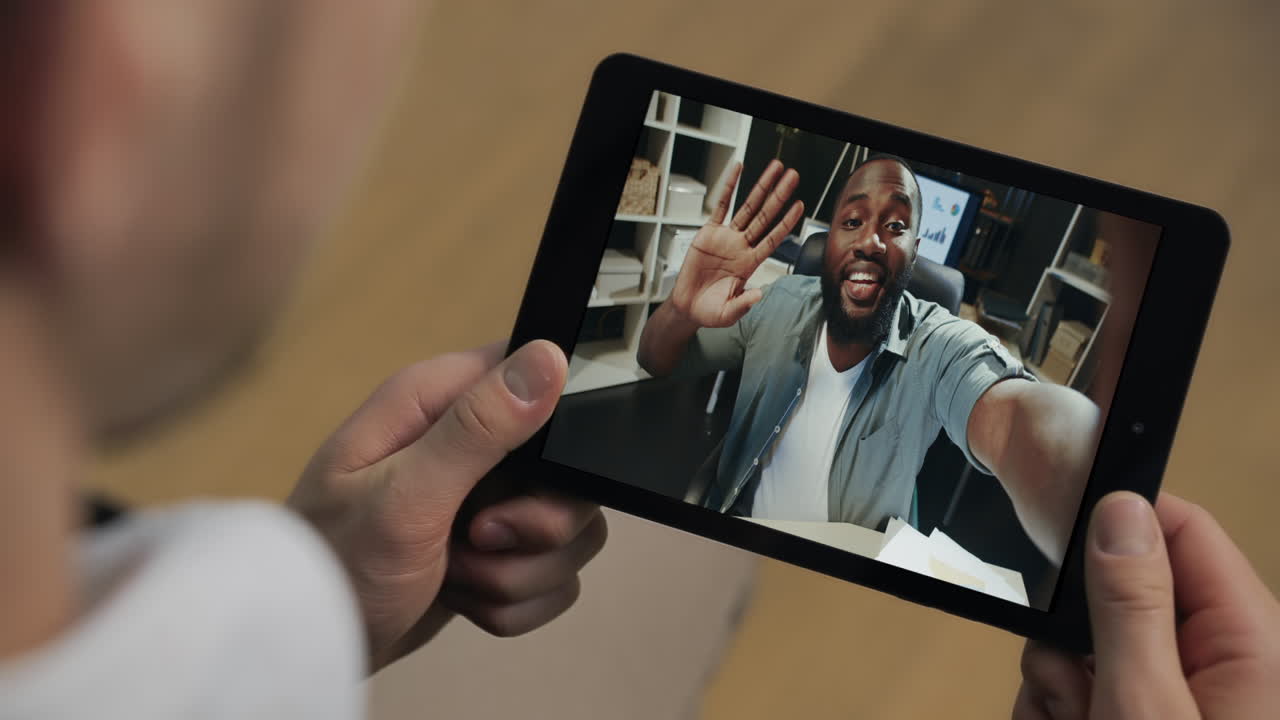 Primo piano di un uomo con tablet che parla online con un collega di startup che tiene in mano un tab in ufficio