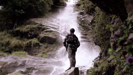 man standing in front of a beautiful waterfall, very relaxing, slow motion shot at day time in norway, europe