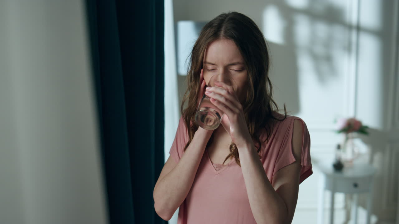 Primo piano di donna malata che beve acqua e soffre di mal di testa. Ragazza stanca che si tocca la testa.