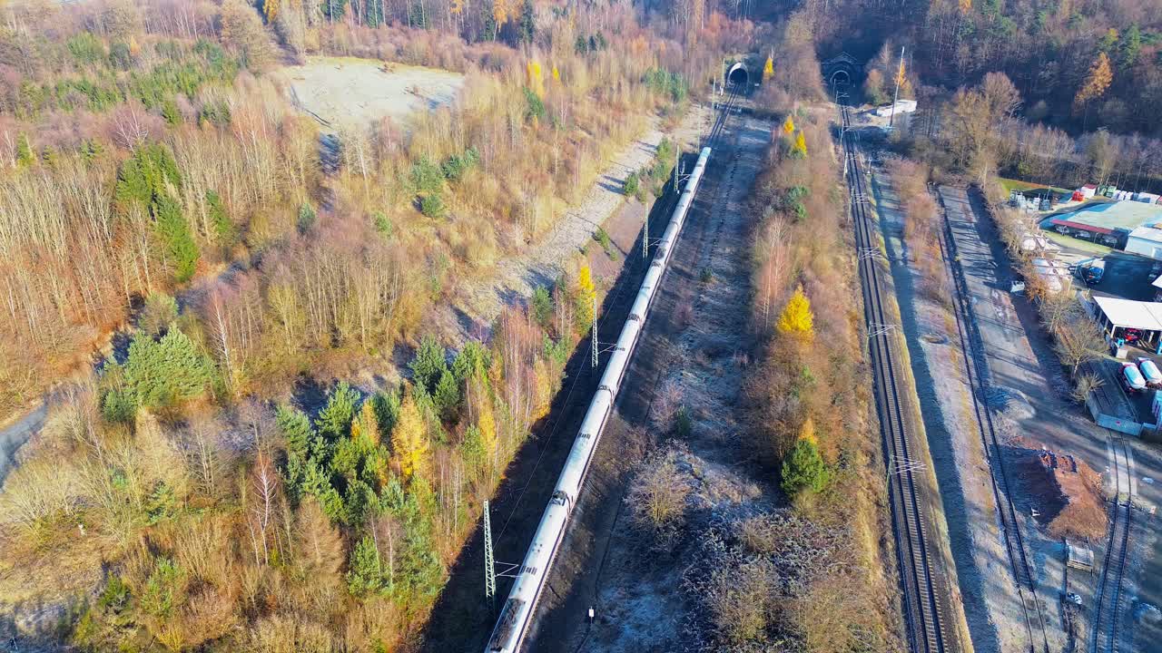 High-speed passenger train exiting railway tunnel through bright frosty winter landscape captured from aerial view