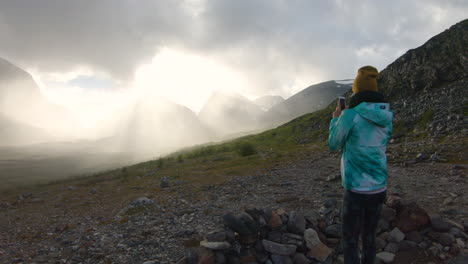 female hiker standing alone and taking photos with her phone of the big mountain kebnekaise at sunset