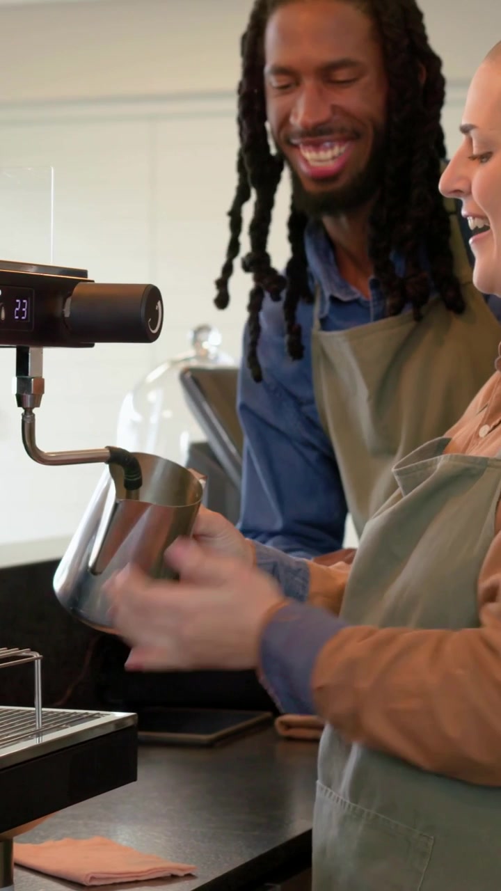 Video verticale: Istruttore che indica, barista con grembiule che monta il latte con lattiera e prepara un caffè al bar.