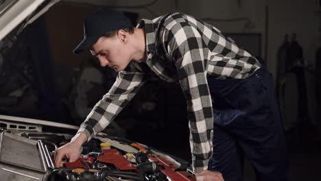 car-service,-repair,-maintenance-and-people-concept---mechanic-man-wearing-work-robe-and-cap-working-at-workshop