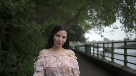 Happy-and-attractive-latina-tourist-with-black-wavy-hair-and-a-floral-dress-walking-and-spinning-in-London's-Thames-walk