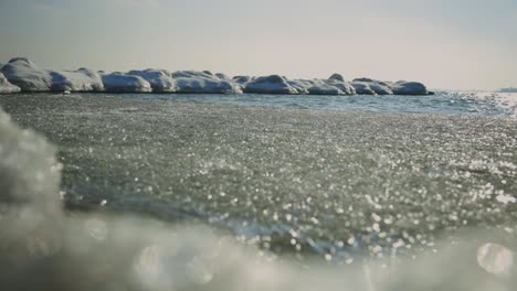 Frosted-Lake-With-Ice-Crystals-Pile-Up-On-The-Shore-With-Rocks-Snow-Covered-In-Background