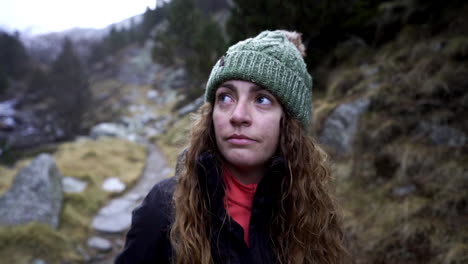 Young-blond-tired-woman-wearing-winter-hat,-looking-around-getting-lost-in-a-mountain-trekking-trails,-slow-motion-expressive-portrait