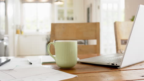 cup, paperworks, smartphone and laptop on table in sunny room at home, slow motion