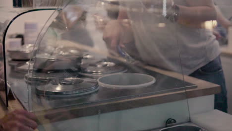 View-of-the-counter-in-the-ice-cream-parlour,-the-seller-puts-ice-cream-from-the-container,-summer-refreshment-with-ice-cream