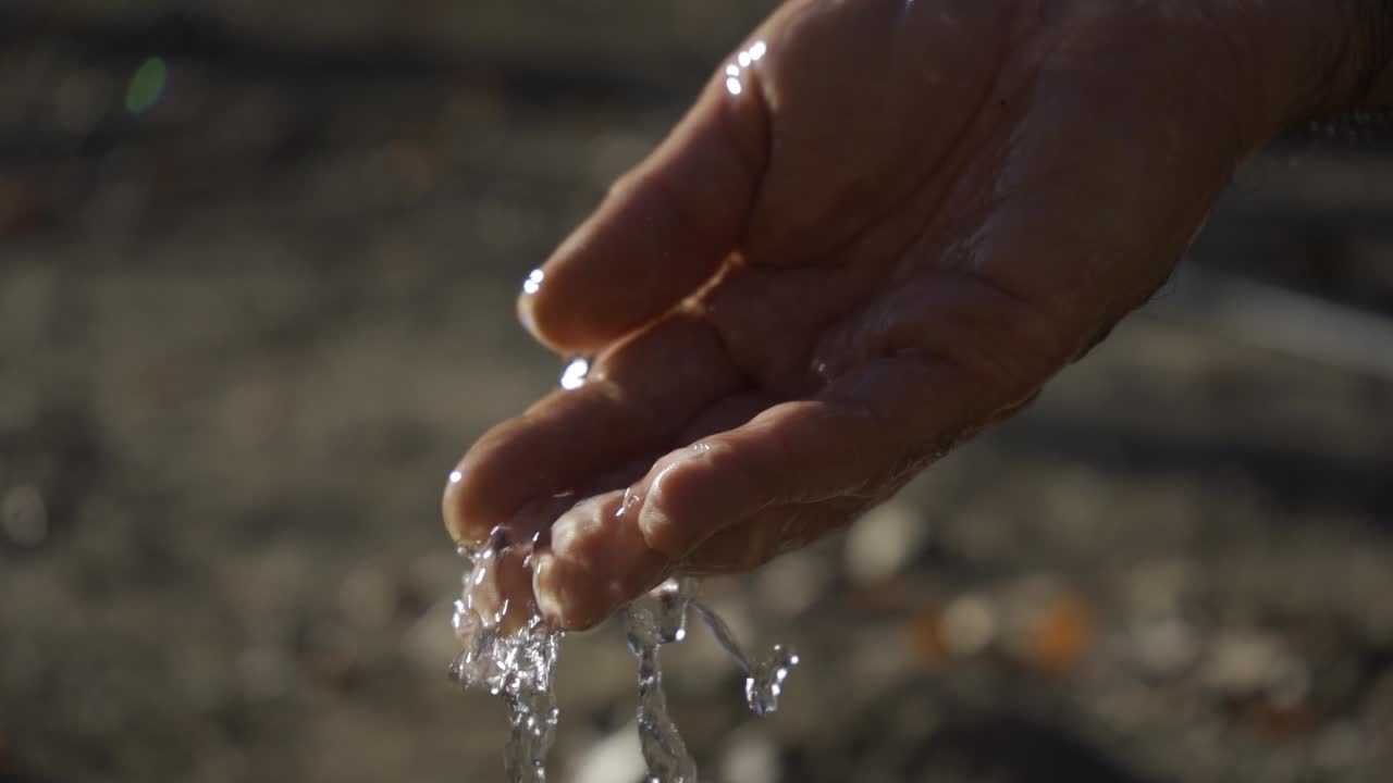 Crystal clear water falling into one hand. Focus on hand. Slow motion.