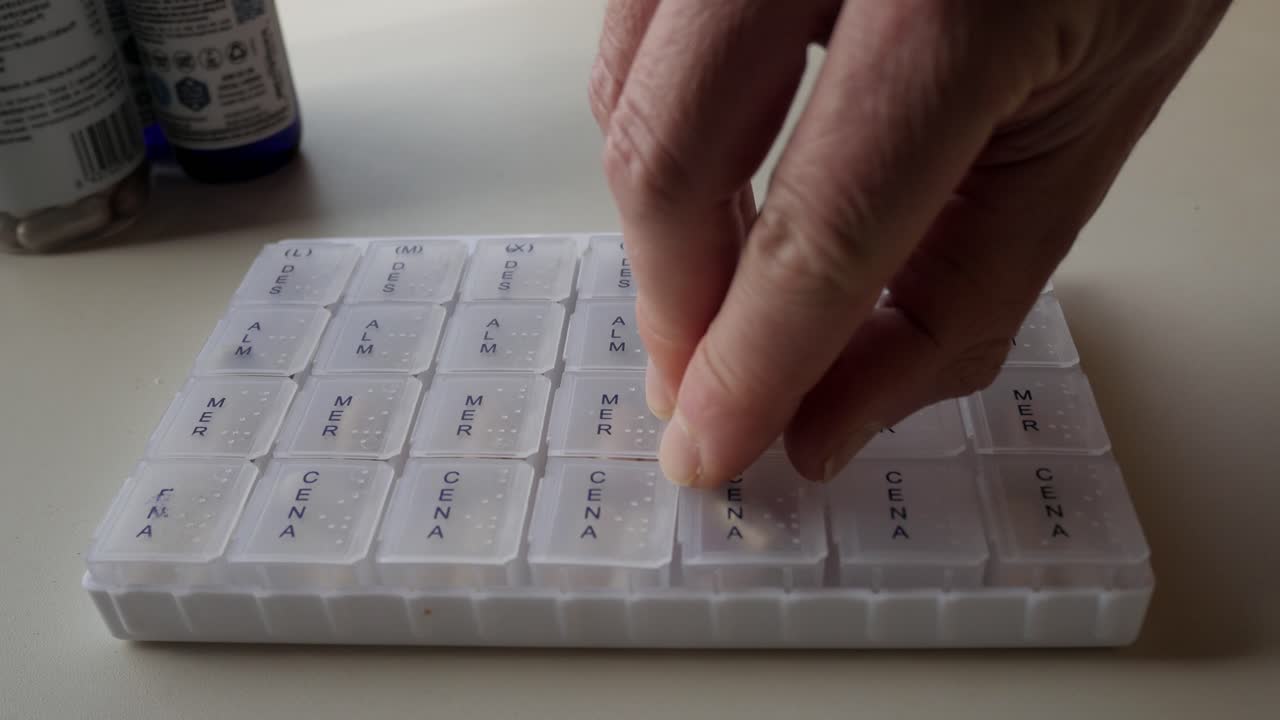 Organizing supplements in weekly pill box, close-up of hand opening evening section