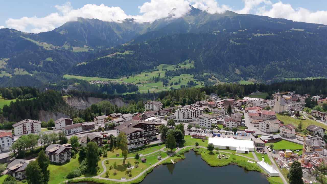 Lag Grond lake in laax City at sunny day. Aerial backwards shot. Summer day with green landscape in famous ski resort town of Switzerland. Wide shot