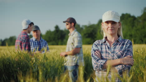 Portrait-Of-A-Young-Woman-Farmer-On-The-Background-Of-The-Field-And-Other-Farmers-Who-Communicate-Be