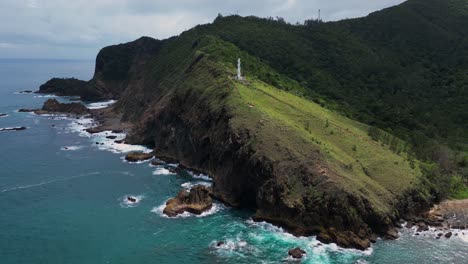 a breathtaking wide shot captures a lighthouse perched atop a small green mountain, overlooking the shore and vast ocean beyond.