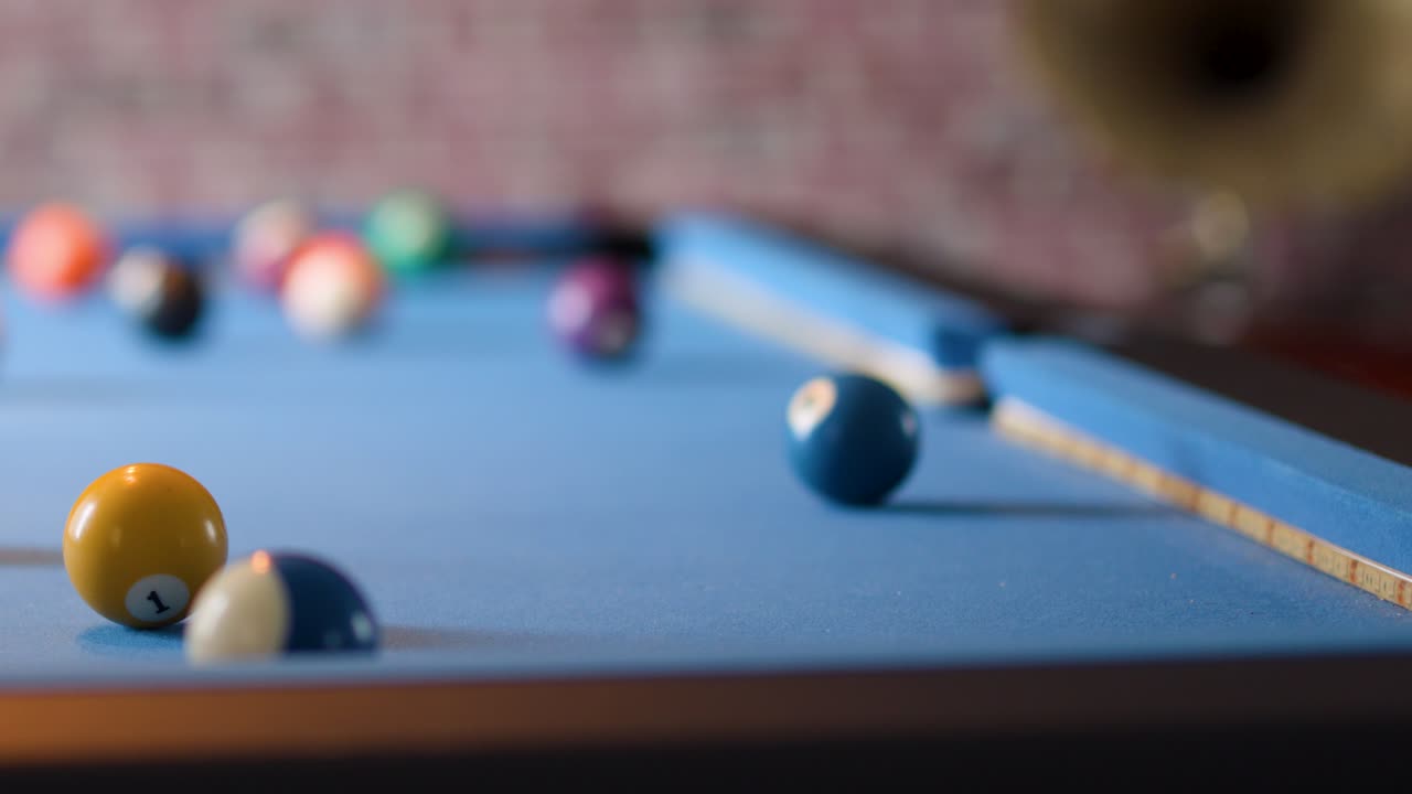 Person prepares to strike billiard balls on blue felt table, shallow focus, warm indoor lighting