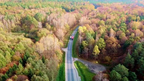 Vista-Aérea-De-Dos-Camiones-Que-Viajan-Por-Carretera-En-Un-Colorido-Bosque-De-Otoño