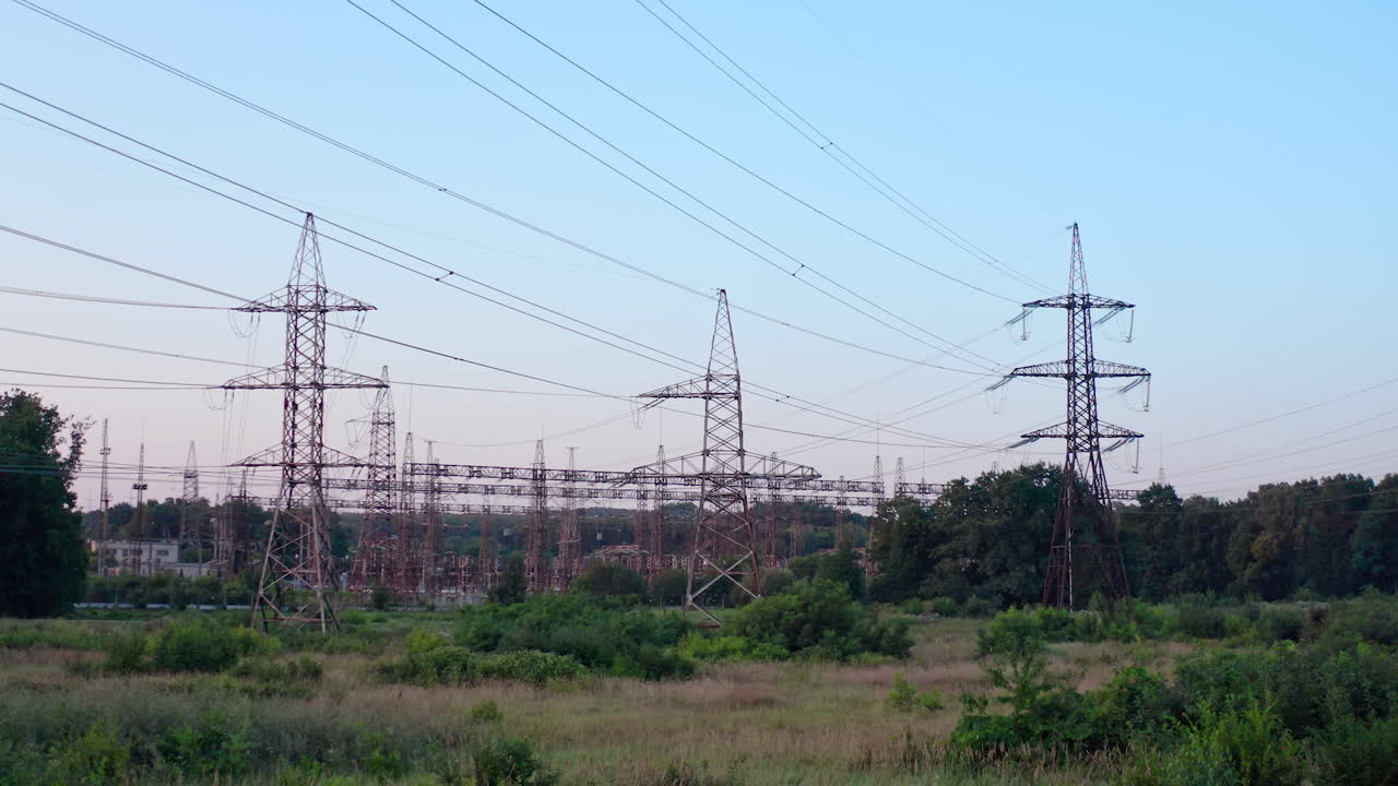 Lots of electricity towers on field. Large power station with many high-voltage electric lines with wires against the sky background. Transmission lines in green nature.