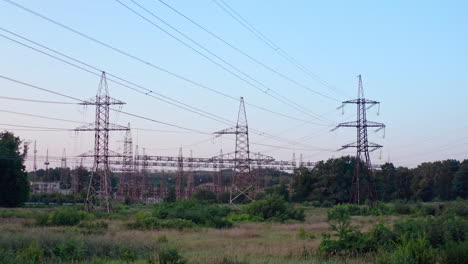 lots of electricity towers on field. large power station with many high-voltage electric lines with wires against the sky background. transmission lines in green nature.