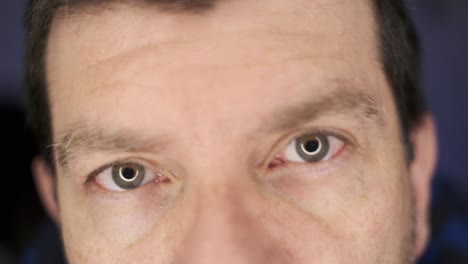 a man looking at the camera in an extreme close-up with eyes going in and out of focus, with a blue, defocused background