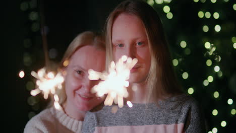 Mom-and-daughter-are-burning-sparklers-on-the-background-of-the-Christmas-tree-at-home