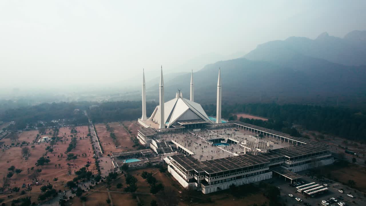 mezquita de faisal en islamabad, mañana tranquila con luz suave, montañas en el fondo, vista aérea