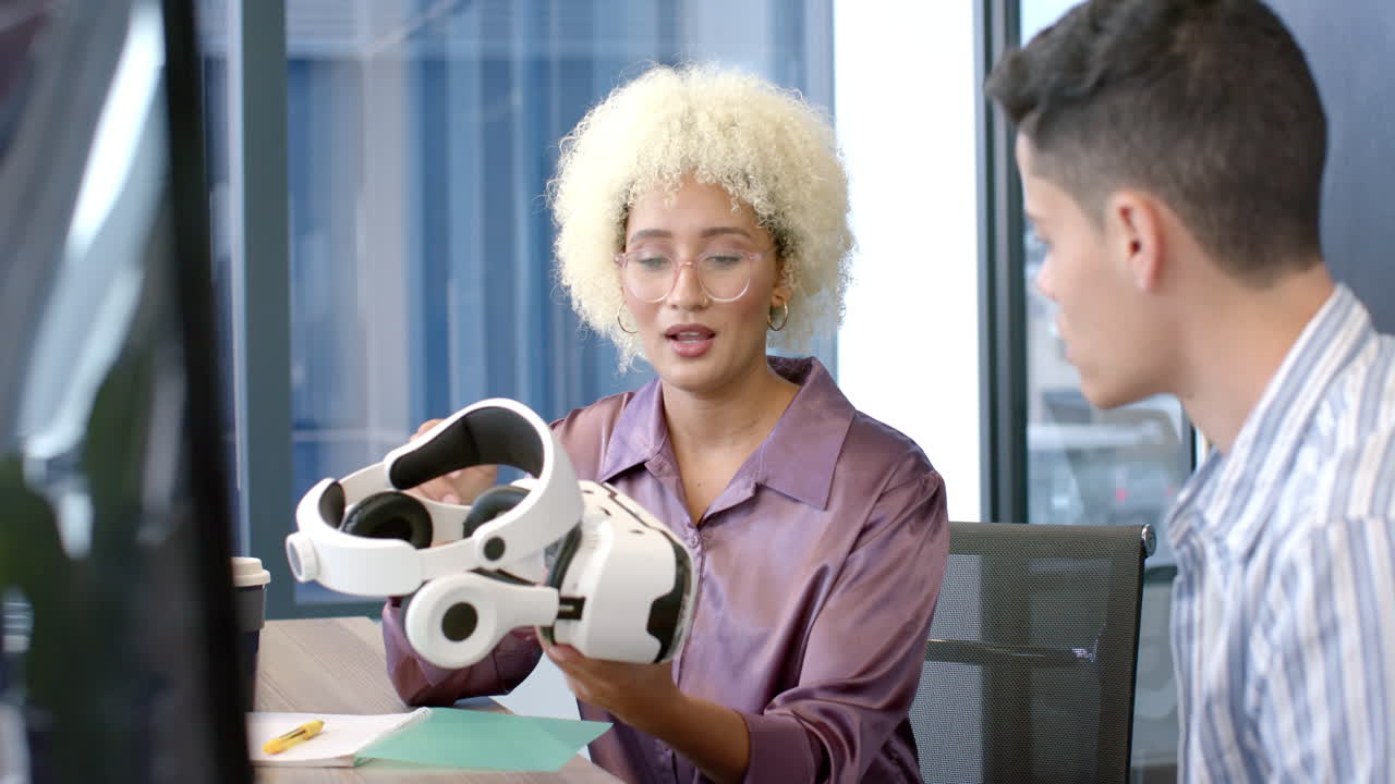 Holding VR headset, woman explaining features to colleague in modern office