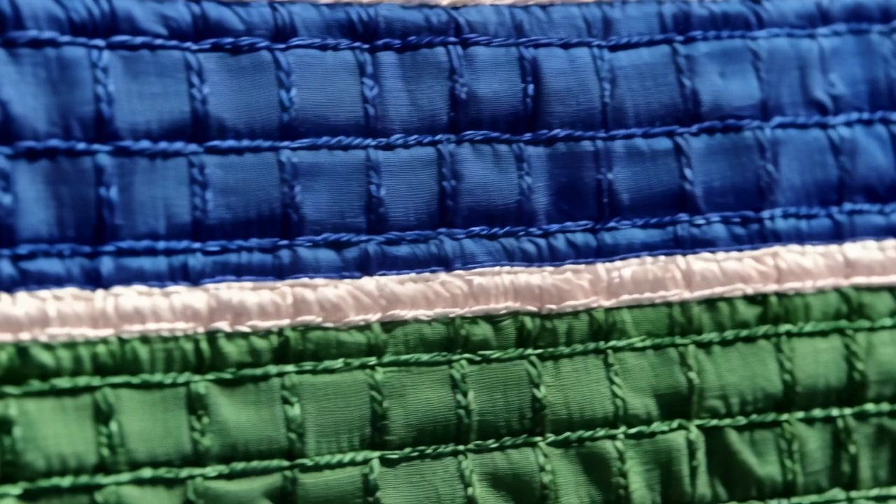 Lowering handheld phone filming quilt indoors, revealing blue green bands and white seam for detail
