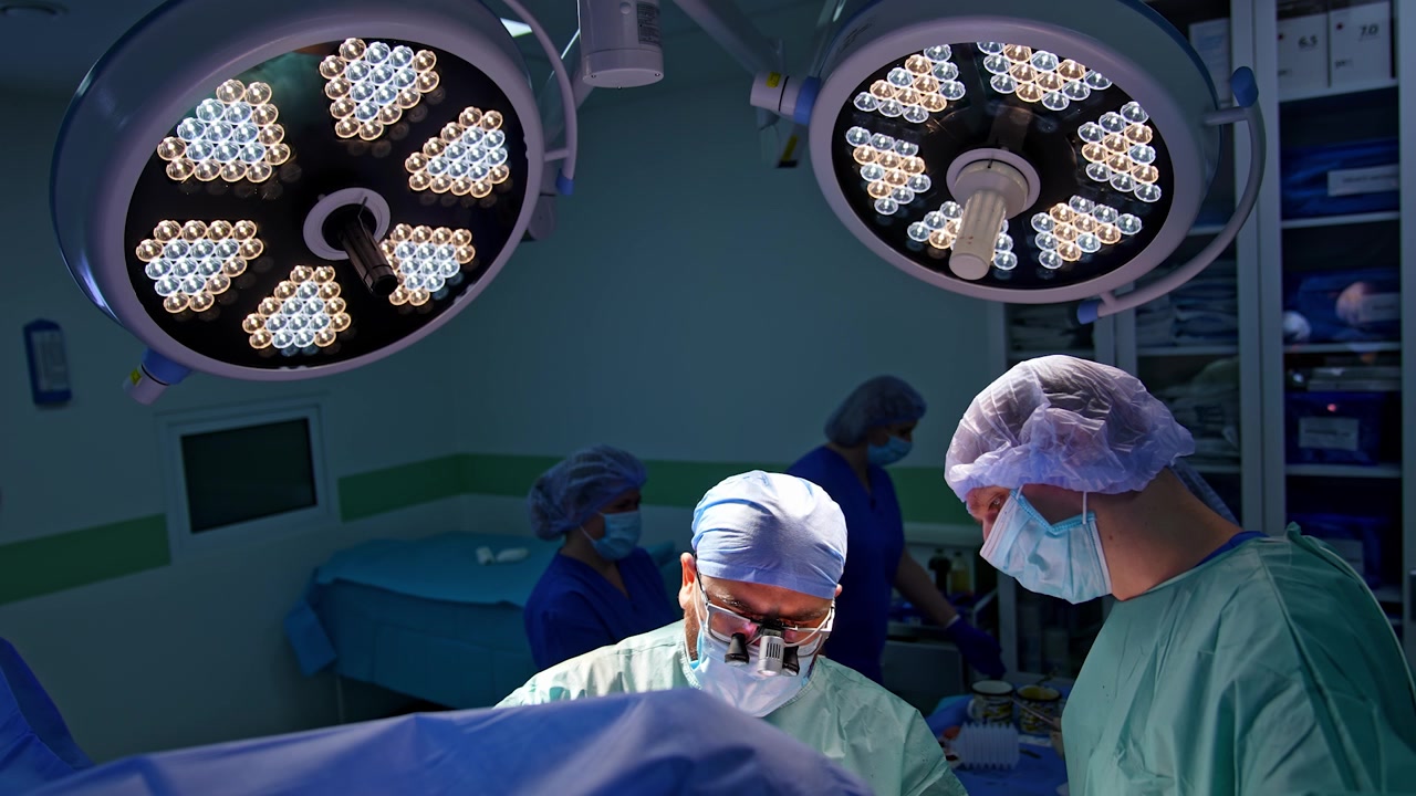 To professionelle kirurger står ved patienten dækket af et blåt lagen. Læger udfører en ortopædisk operation. Højt vinkelperspektiv på medicinerne under skarpe runde lamper
