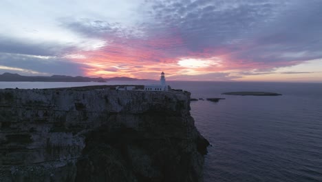 El-Dron-Aéreo-Del-Horizonte-Del-Atardecer-De-Fuego-Se-Acerca-Al-Acantilado-Del-Faro-De-Cavalleria,-Al-Norte-De-La-Arquitectura-De-Menorca-En-El-Borde-Del-Océano