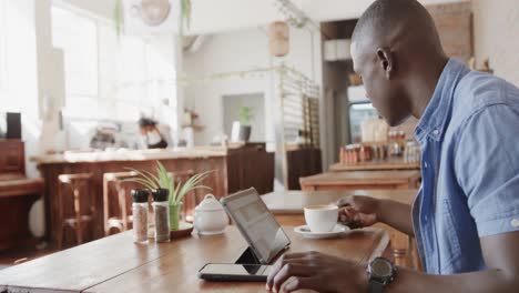 hombre afroamericano feliz usando una tableta y bebiendo café en una cafetería, cámara lenta