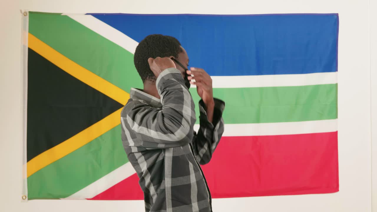 African man puts on mask in front of South African flag