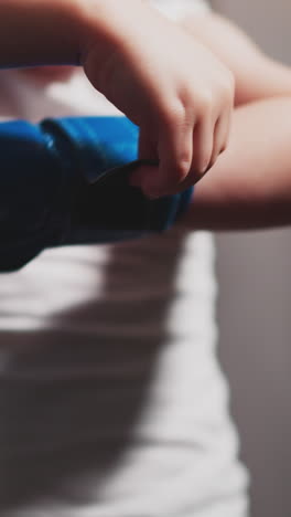 active little boy fixes blue boxing glove on hand preparing for fight. motivated toddler ready for boxing against dark curtain closeup slow motion