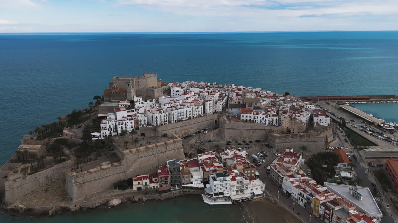Curved aerial of Castell de Peniscola fortress with sea establishings and waterfront buildings