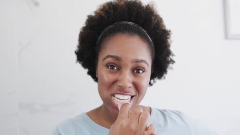 Portrait-of-happy-african-american-woman-brushing-teeth-and-smiling-in-bathroom,-slow-motion