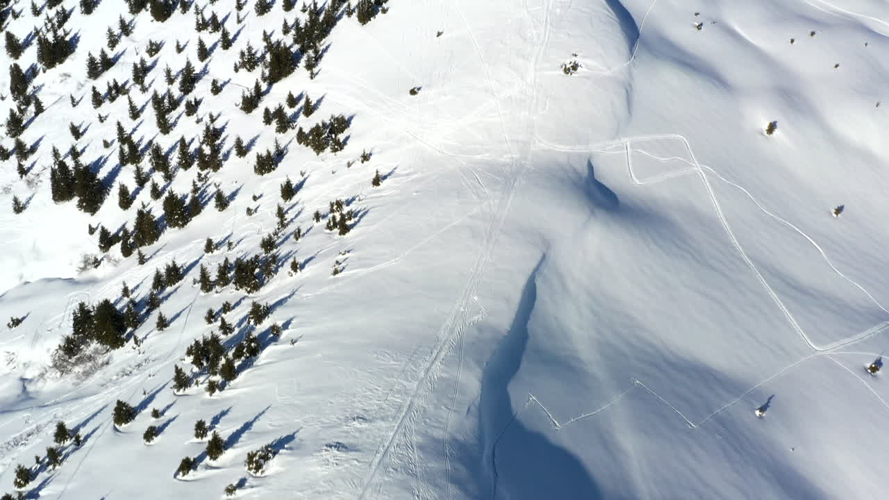 vista aérea volando a lo largo de una cresta de montaña cubierta de nieve antes de subir para revelar un fondo de montaña en la nieve en un día soleado