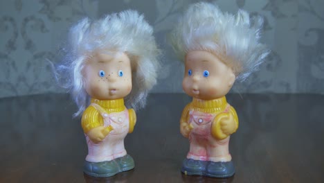 two toy twin dolls stand on a wooden table