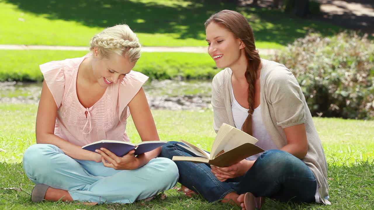 Two ladies reading in the park as they then look at the camera