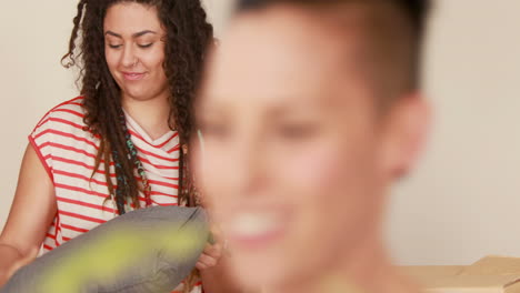 Pareja-De-Lesbianas-Sonriente-Desempacando-Caja-De-Cartón