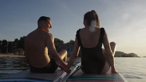 couple holding hands on paddleboards at sunset