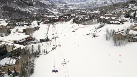 aerial drone shot of chairlift and people skiing and snowboarding in aspen, colorado.