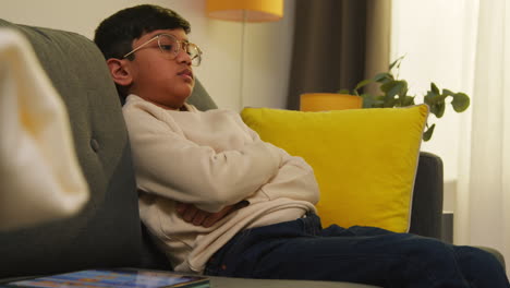 young boy sitting on sofa at home fed up with playing games or streaming onto digital tablet 1