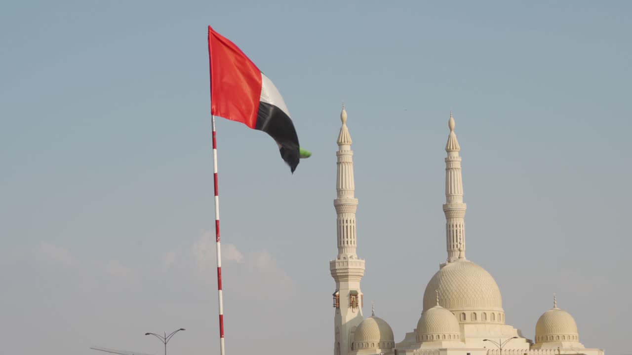bandera de los emiratos árabes unidos y mezquita de la universidad al qasimia contra el cielo azul brillante en la ciudad de sharjah - tiro medio