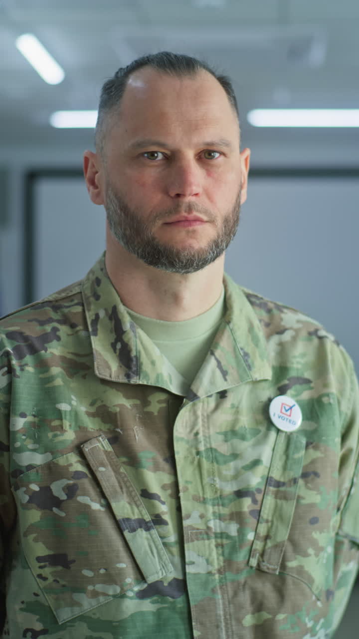 retrato de soldado masculino, votante de las elecciones de los estados unidos de américa. hombre en uniforme de camuflaje se encuentra en una estación de votación moderna y mira a la cámara. fondo con cabinas de votación. concepto de deber cívico.