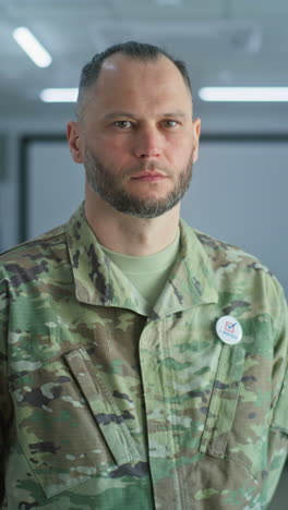 portrait of male soldier, united states of america elections voter. man in camouflage uniform stands in a modern polling station and looks at camera. background with voting booths. civic duty concept.