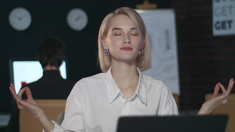 Business-woman-meditating-in-yoga-pose-front-computer-table-in-night-office